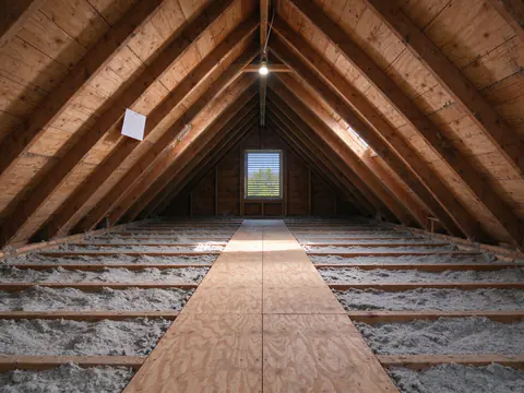 A sunlit vented attic over a Los Angeles bungalow with old porcelain knob runs on the ceiling joists and a clear floor ready for insulation