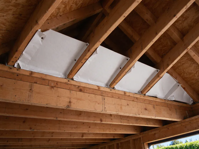 White vent baffles stapled between the rafters at the eaves of an attic